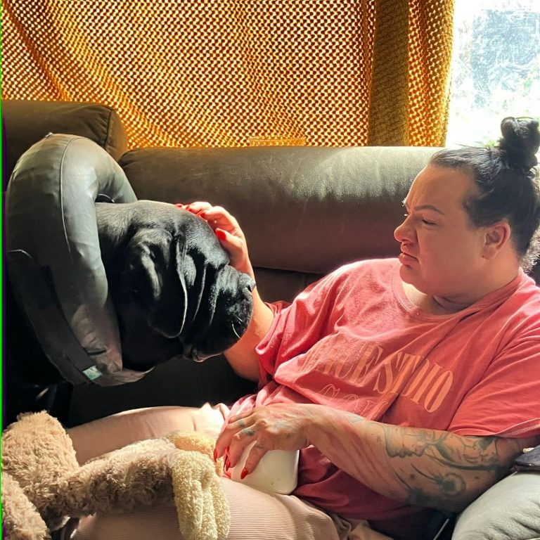 A person gently petting a black dog while sitting on a couch.